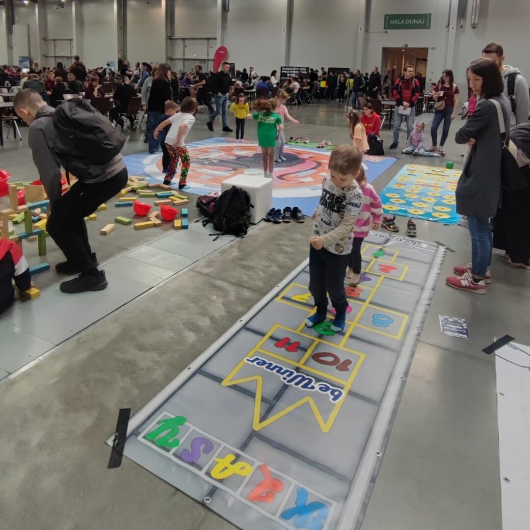 Gra korytarzowa „Klasy” z kolorowymi numerami – dzieci skaczą po polach, rozwijając sprawność i równowagę.